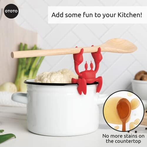 Red crab-shaped spoon holder on white pot with wooden spoon and cauliflower.